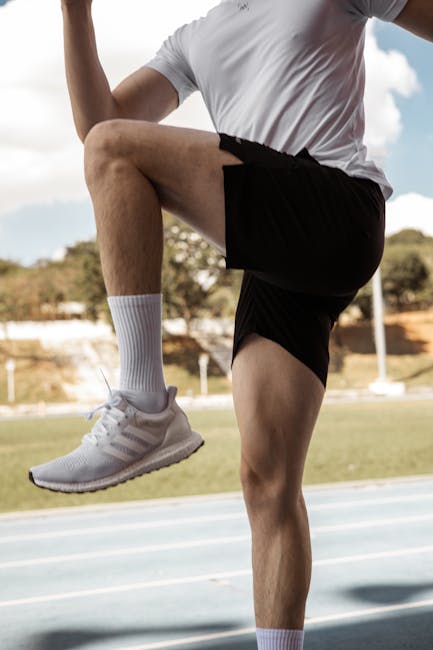 Man in athletic wear exercising on an outdoor track under a clear sky.
